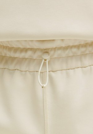 Beige joggingsbroek met een trekkoord in de taille, zachte stof en opgehaald elastiek bij de tailleband voor een verstelbare pasvorm en comfort.