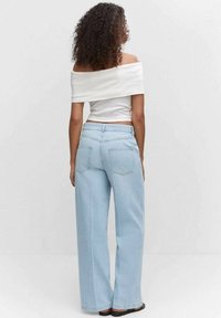 Jeans anchos de color azul claro con bolsillos traseros, combinados con una blusa blanca sin mangas, vistos desde atrás sobre un fondo neutro.