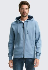 Lichtblauwe zip-up hoodie met een trekkoordkap, voorzakken en ribgebreide manchetten. Zacht materiaal met een gladde textuur en contrasterende marineblauwe binnenkant.
