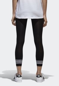 Černé legíny s texturovaným žebrováním, s bílými pruhy na lemu. V kombinaci s bílými sportovními teniskami.