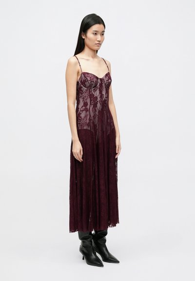 Bordové čipkované šaty s tenkými ramienkami, zdobené kvetinovými vzormi a plynúcim spodkom. Kombinujte s čiernymi čižmami s špicatou špičkou.