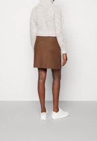 Bruine wollenblend rok met een aansluitende pasvorm, voorzien van achterzakken. Gepaard met een gestructureerde lichte trui en witte sneakers.