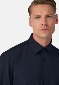 Camicia a maniche lunghe blu navy con colletto strutturato, apertura con bottoni e texture liscia, caratterizzata da dettagli di cucitura sottili sulle spalle.