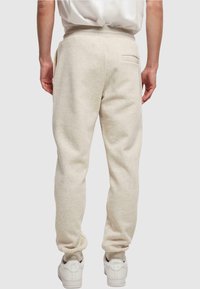 Beige sweatpants gemaakt van zacht materiaal, met een taps toelopende pasvorm, een elastische tailleband en een achterzak. Gepaard met witte sneakers.