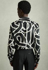 Camicia nera con motivi astratti a linee bianche, con maniche lunghe e colletto a punta, realizzata in tessuto morbido.