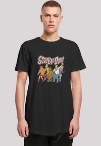 Svart bomull t-skjorte med et fargerikt grafisk trykk av tegneseriefigurer fra "Scooby-Doo" på forsiden. Korte ermer, rund hals.