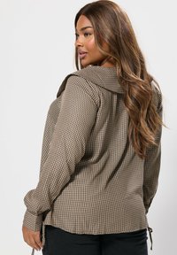 Camicia a quadri marrone e beige con maniche lunghe e un ampio colletto, caratterizzata da una vestibilità rilassata, lacci laterali e una texture morbida.