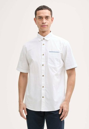 Chemise blanche à manches courtes en coton avec un col boutonné, des boutons dorés et une poche poitrine unique agrémentée d'une rayure bleue.