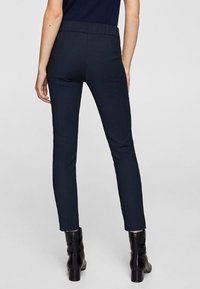 Marineblauwe, taps toelopende broek met een gladde textuur en een elastische tailleband, met minimale naden en een gestroomlijnde silhouet.