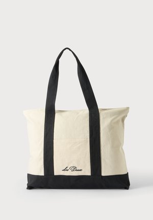 Canvas-totepose med lange sorte håndtag, sort bundkant og frontlomme med "Les Deux" logo i sort skrift.