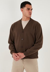 Cardigan lavorato a maglia marrone con scollatura a V, chiusura con cinque bottoni e maniche lunghe. Tessuto leggero con polsini e corpo a coste.