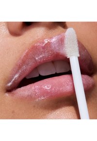 Lepomade med en blank, transparent rosa nyanse og en subtil glans. En hvit applikatorstav påfører produktet på fyldige, glansfulle lepper.
