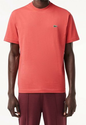 Koralowa bawełniana koszulka z krótkim rękawem i okrągłym dekoltem; ma małe zielone haftowane logo na piersi.