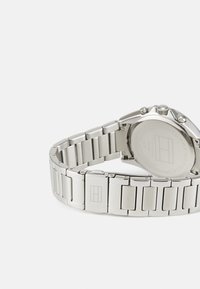 Montre en acier inoxydable argenté avec un bracelet à maillons, présentant un boîtier rond et une texture lisse et polie. Logo sur la boucle.