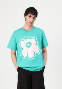 Turquoise cotton t-shirt featuring a large pink flower graphic with stylized text. Short sleeves and a round neck design.