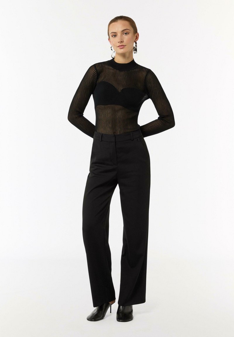 Czarna siateczkowa bluzka z długim rękawem i pionowymi paskami, w zestawieniu z czarnymi spodniami o wysokim stanie. Całość uzupełniają szpilki.