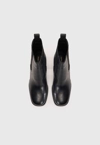 Un paio di stivali Chelsea in pelle nera con pannelli laterali elasticizzati e linguette, mostrati dall'alto su uno sfondo bianco.