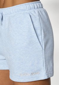 Calções de algodão azul claro com um cós elástico, bolsos laterais e um pequeno logo branco "BJÖRN BORG" na bainha inferior. Textura suave.