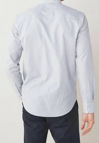 Chemise à rayures bleues claires et blanches à manches longues avec un ourlet incurvé et des poignets boutonnés. Texture de tissu lisse, design de col classique.