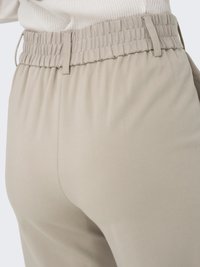 Pantalons de détente beiges et extensibles avec une taille smockée et des poches latérales ; texture lisse et coupe ample, vus de côté.