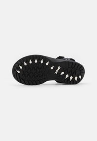 Black sandal sole with deep grooves for traction, featuring white rubber spikes, and a textured surface with raised patterns.
