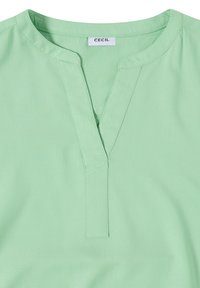 Blouse vert clair avec un col rond fendu et une patte verticale cousue, avec une étiquette de marque « CECIL » à l'intérieur du col.