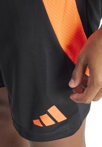 Schwarze Sportshorts mit einem orangen strukturierten Einsatz und drei diagonalen Streifen am Saum. Glattes Material mit einer körpernahen Passform.