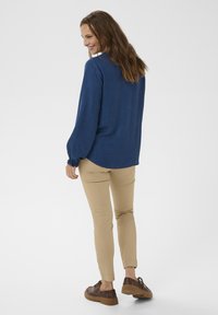 Cămașă albastră cu mâneci lungi dintr-un material texturat, manșete elastice; asortată cu pantaloni bej cu croială slim și pantofi maro. Design curat și minimal.