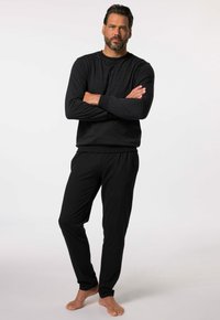 Top de manga larga a rayas negras y grises y pantalones negros, hechos de una tela suave con cinturilla elástica. Posición descalzo frente a un fondo liso.