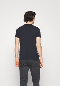 Mörkblå kortärmad T-shirt i bomull med rund halsringning. Bärs tillsammans med mörka byxor, vilket visar en figursydd silhuett från baksidan.