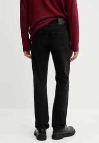 Jeans in denim neri presentano una vestibilità dritta e tasche posteriori, abbinati a una camicia a maniche lunghe bordeaux e scarpe nere.