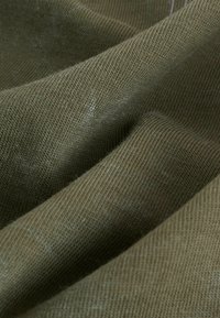 Olívová tkanina s textúrovaným, ryhovaným vzorom; mäkký a mierne chlpatej vzhľadu. Materiál vykazuje jemné variácie v farbe a textúre.