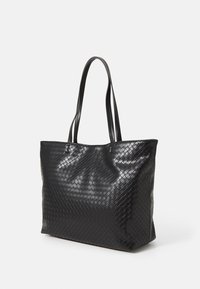 Černá taška přes rameno s tkanou koženou strukturou a dlouhými dvojitými uchy, stojící vzpřímeně na uniformním bílém pozadí.