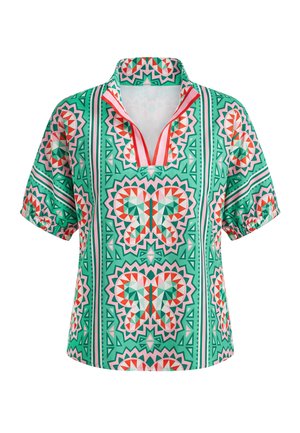 Blouse verte à manches courtes avec motifs géométriques de papillons en rose, rouge et blanc, avec un col fendu bordé de rouge.
