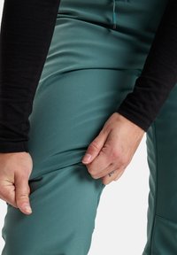 Türkise Sporthosen mit glatter Textur, verstellbarem Kordelzug und körpernaher Passform, die gerade von einer Hand angepasst werden.