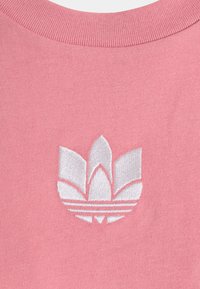 Pink sweatshirt fabric with a ribbed neckline. Features a white embroidered logo resembling three petals and three stripes at the bottom.