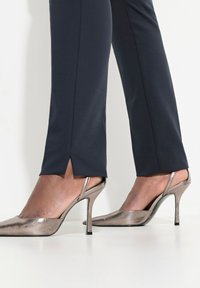 Navy tailormade broek met een split aan de zoom, gecombineerd met metallic bronzen stiletto hakken, met een puntige neus en een slingback ontwerp.