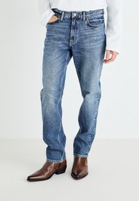 Light blue denim jeans with a relaxed fit, five-pocket design, and subtle fading, paired with brown leather pointed-toe boots.