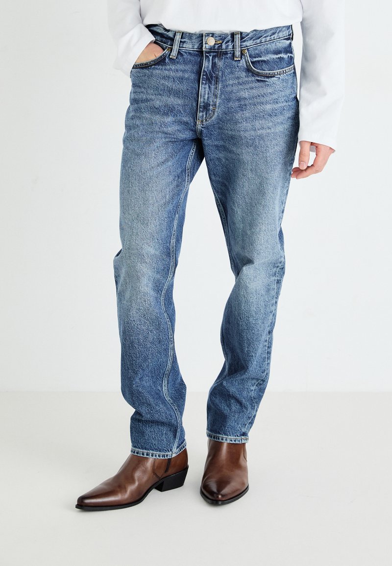 Light blue denim jeans with a relaxed fit, five-pocket design, and subtle fading, paired with brown leather pointed-toe boots.