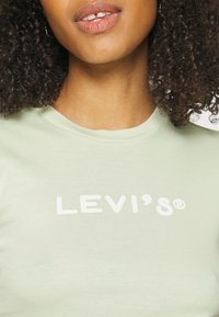 Lysegrøn bomulds T-shirt med korte ærmer, der har et hvidt grafisk logo "LEVI'S®" over brystet i en fed, moderne skrifttype.