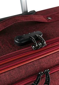 Maleta de tela roja con doble cremallera, mecanismo de bloqueo negro y asa retráctil. Superficie texturizada con detalles en contraste.