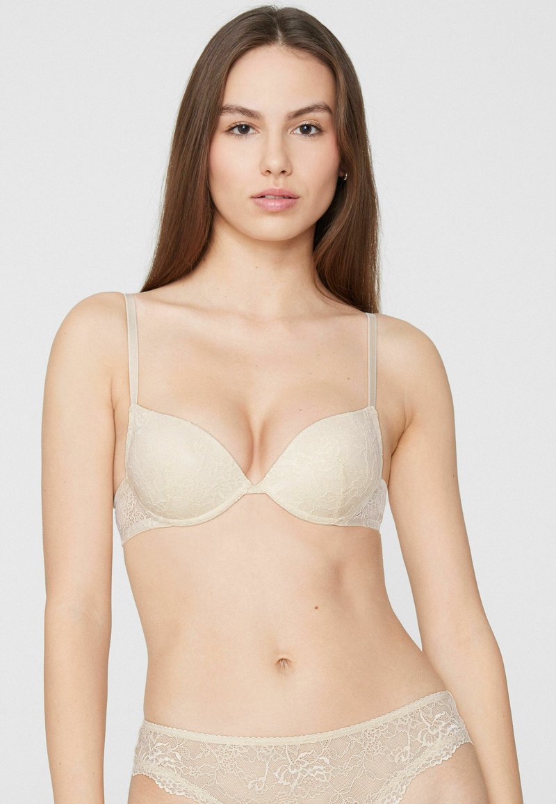 Reggiseno in pizzo beige chiaro con design liscio e imbottito, dotato di spalline sottili regolabili e scollatura profonda per una migliore modellatura.