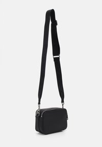 Čierna crossbody taška s textúrovaným povrchom, dvojitým zipsom a nastaviteľným popruhom s logom. Kompaktný obdĺžnikový tvar.