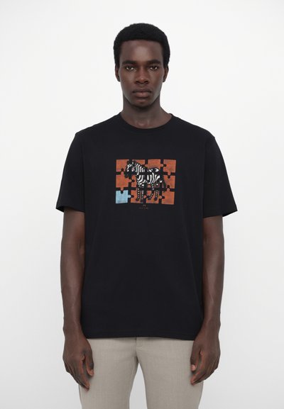 Tricou negru din bumbac cu un grafic de zebră pe un fundal cu un model de puzzle în nuanțe de portocalie și albastră. Mânici scurte și un gât rotund.