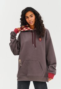 Tmavosivá voľná mikina s kapucňou so šachovnicovým červeným a béžovým podšívkou, vyšívaným logom, prednou vreckom a kontrastnými červenými manžetami.