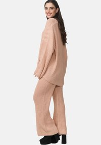 Ljusrosa stickad tvådelad outfit med en lös passform, ribbad tröja och vida byxor. Svarta plattformsskor fulländar looken.