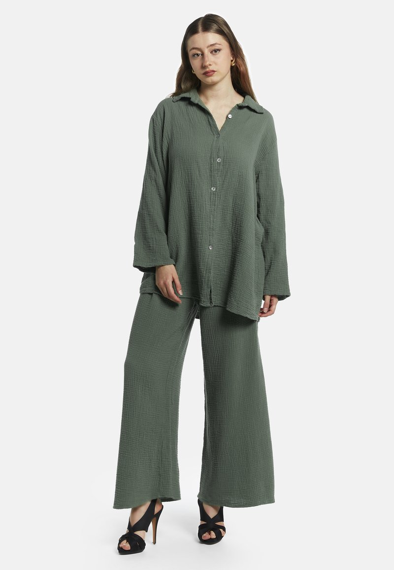 Grøn to-delt outfit lavet af tekstureret stof. Toppen har en knaplukning og en afslappet pasform, som er parret med brede bukser og sorte hæle.