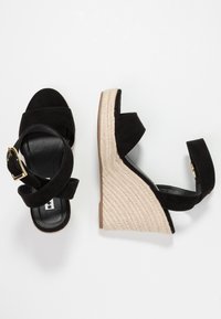 Sandales compensées en daim noir avec talon en corde tressée de style espadrille. Design à bride de cheville avec détail de boucle dorée.