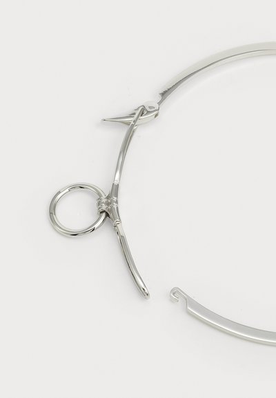 Lunettes en métal argenté avec un lien circulaire, une monture élégante et des extrémités pointues. Texture lisse avec finition brillante.