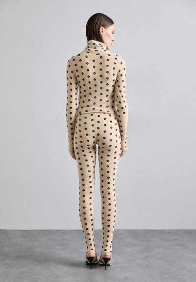 Completo in maglia beige a due pezzi, composto da un dolcevita aderente e leggings, decorato con motivi floreali neri su tutto il tessuto. Scarpe con tacco alto.